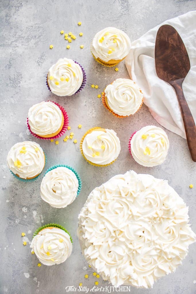 Overhead of Fluffy Buttercream frosting on cupcakes and cake with wooden spatula.