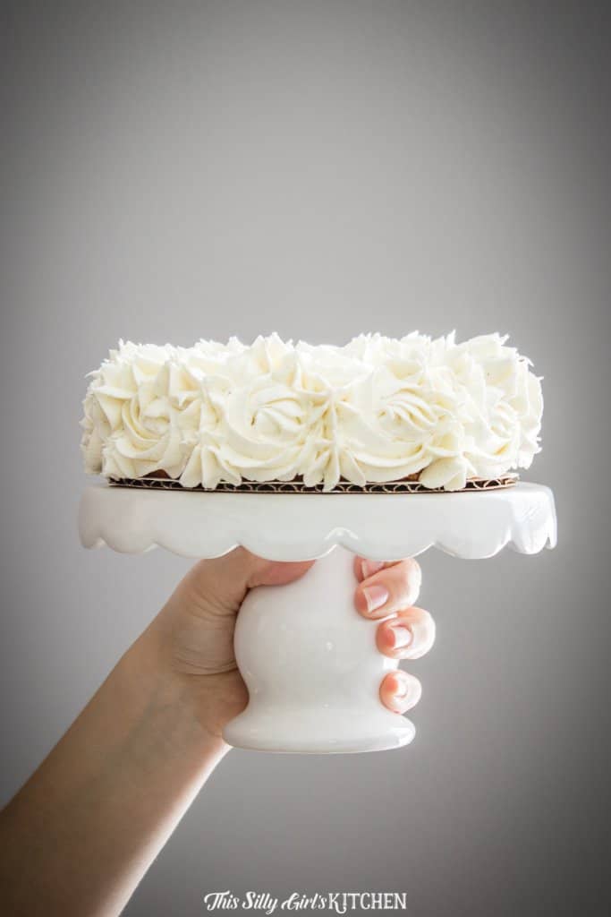Hand holding up cake stand with a frosted cake.