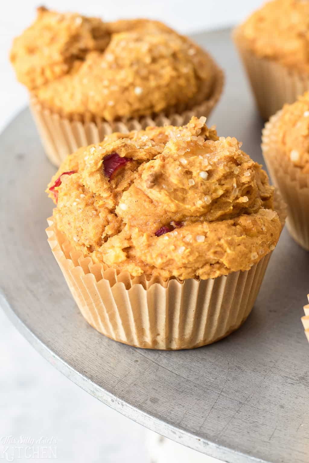 Pumpkin Muffins with cranberries cooling on a baking sheet with scattered fresh cranberries.