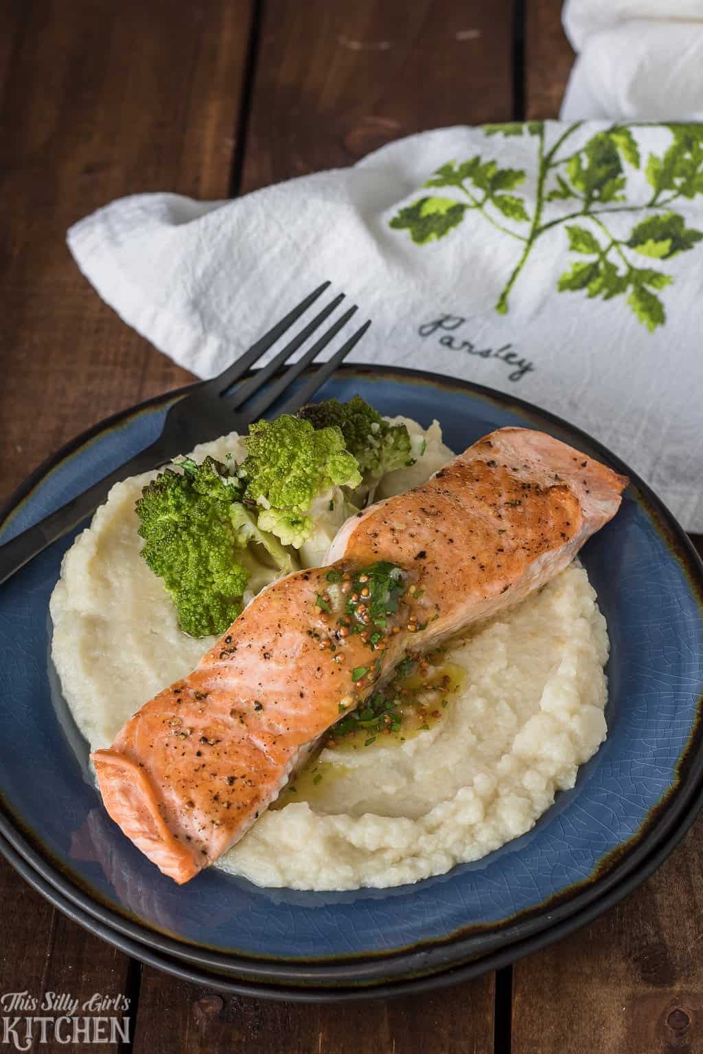 A fillet of pan seared salmon over mashed cauliflower garnished with parsley and maple vinaigrette.