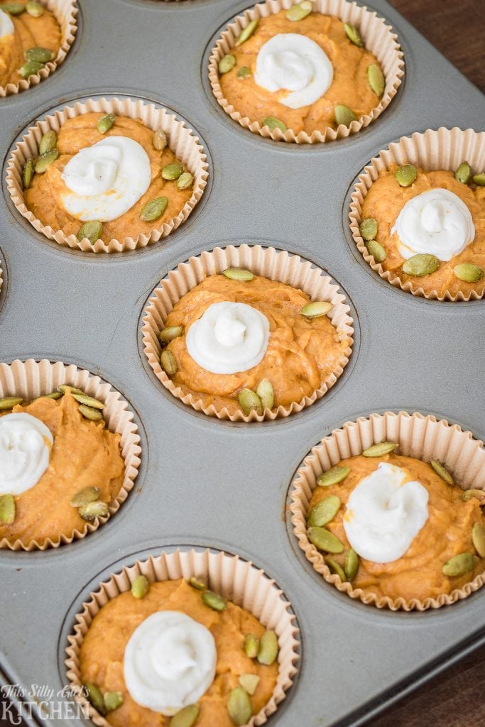 Batter and cream cheese with pumpkin seeds in muffin tin.