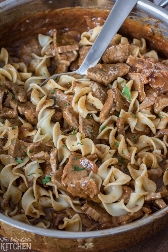 Noodles mixed in with Steakhouse Beef Tips with spoon in pan