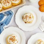 Frosted pumpkin cinnamon rolls on white plates with a glass of milk.