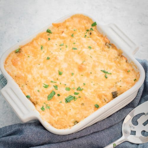 A scoop of cheesy zucchini rice casserole lifted from a baking dish with a golden, bubbly cheese topping.