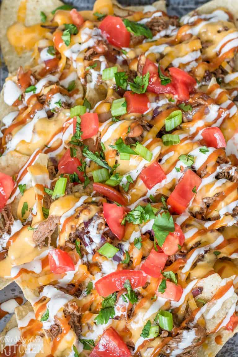 A sheet tray of loaded BBQ beef nachos with cheese sauce, tomatoes, and scallions.