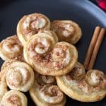 A plate of cinnamon cream cheese palmiers with cinnamon sticks on a plaid napkin.