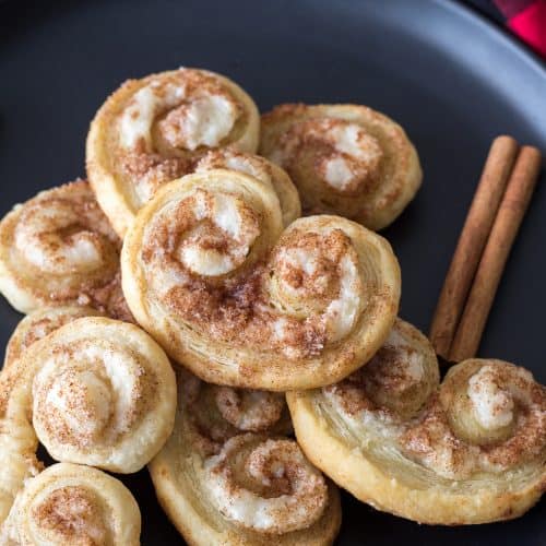 A plate of cinnamon cream cheese palmiers with cinnamon sticks on a plaid napkin.