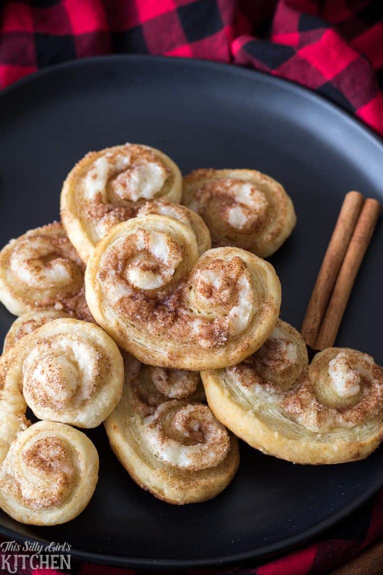 A plate of cinnamon cream cheese palmiers with cinnamon sticks on a plaid napkin.