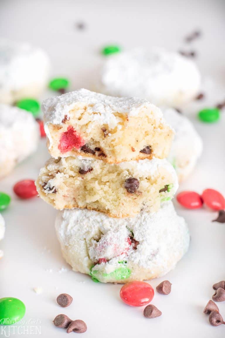A stack of Snowball Cookies with the top cookie broken open showing chocolate chips and candy pieces inside.