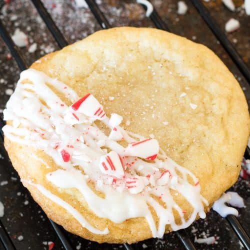 A white chocolate peppermint cookie drizzled with white chocolate and crushed candy cane on a cooling rack.