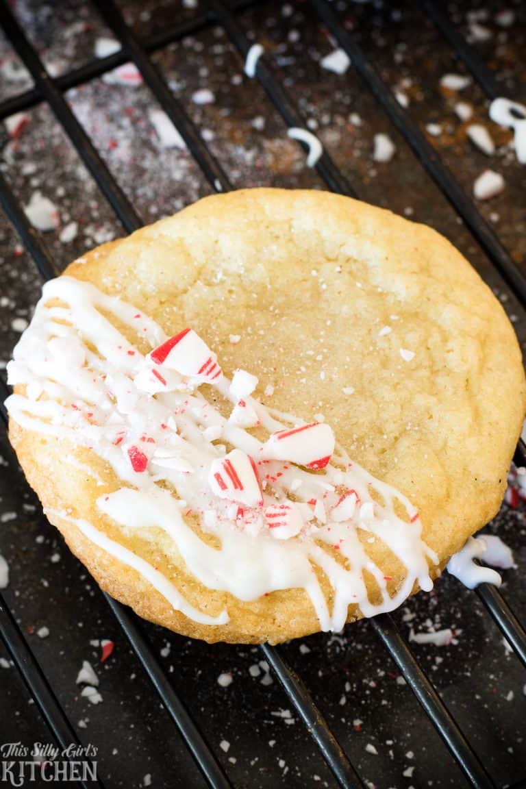 A white chocolate peppermint cookie drizzled with white chocolate and crushed candy cane on a cooling rack.