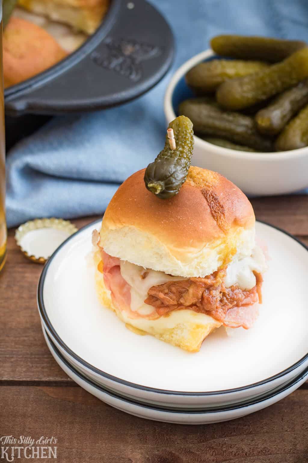 One Baked Cuban Sandwich on white plate with a bowl of pickles in backgroung.