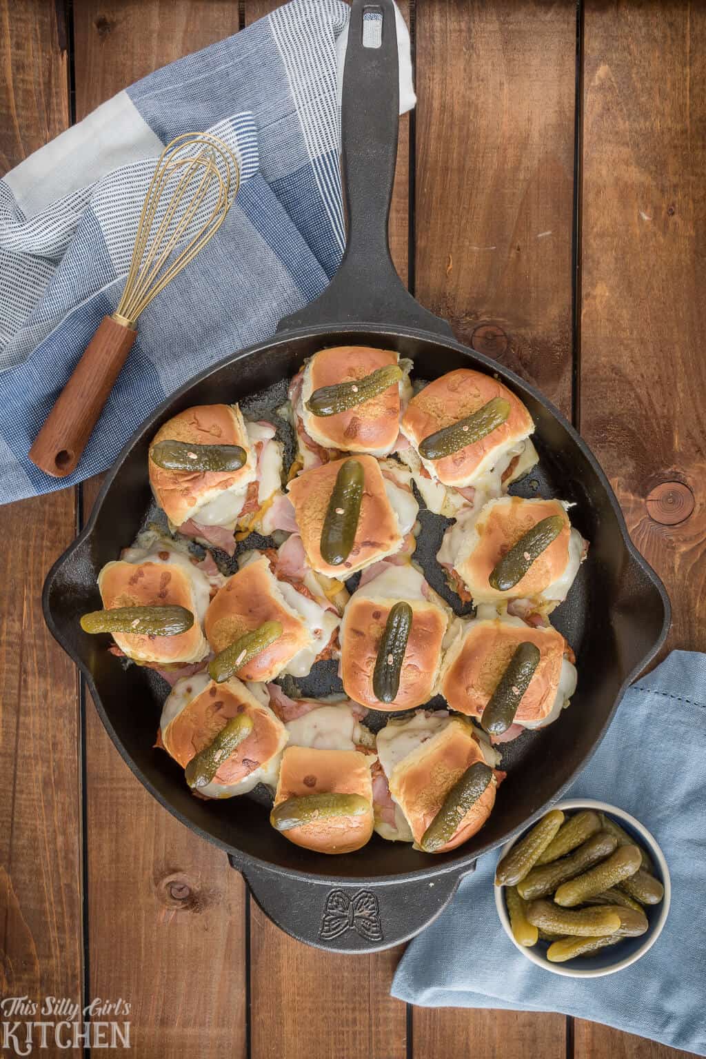 Overhead of sandwiches in cast iron skillet topped with pickles.