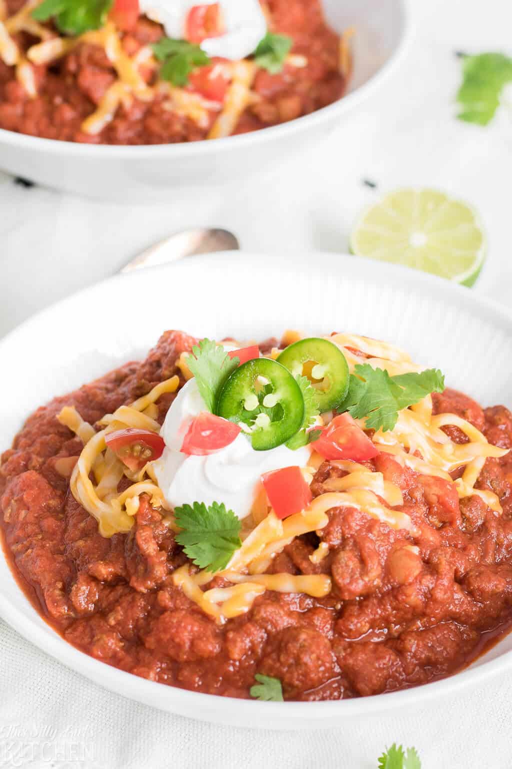 Slow Cooker Chili in white bowl with various toppings