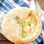 An individual chicken pot pie with a flaky golden crust cut open to show the creamy filling with peas and carrots.