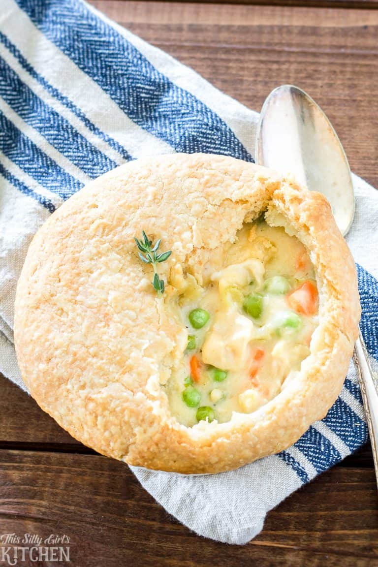An individual chicken pot pie with a flaky golden crust cut open to show the creamy filling with peas and carrots.