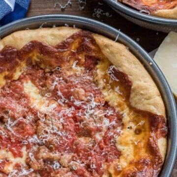 A Chicago deep dish pizza in a round pan with a thick golden crust, gooey cheese, sausage, and chunky tomato sauce.