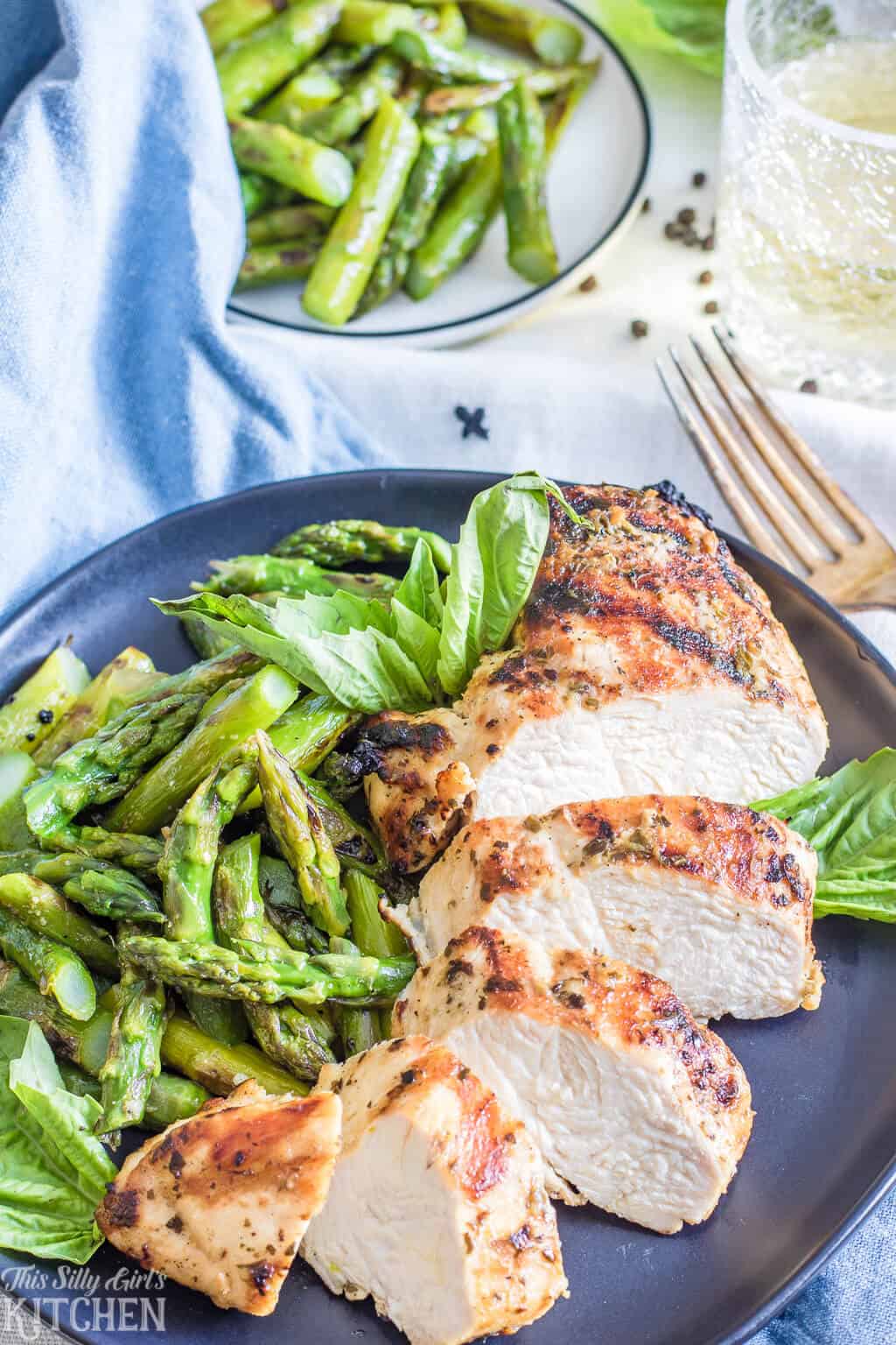 Pesto Chicken Marinade on cut up grilled chicken on plate with asparagus