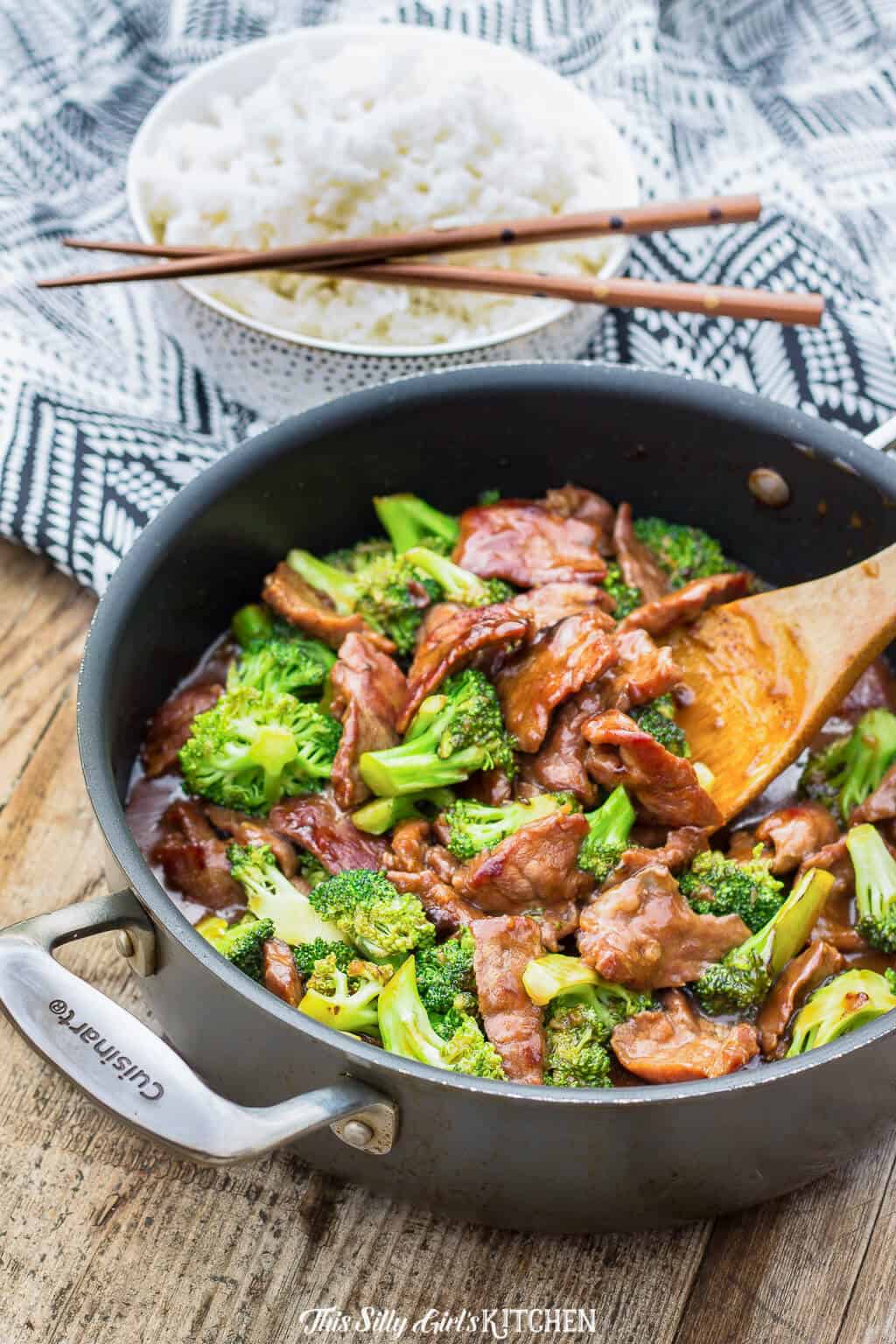 Beef and Broccoli in pan with bowl of rice in background