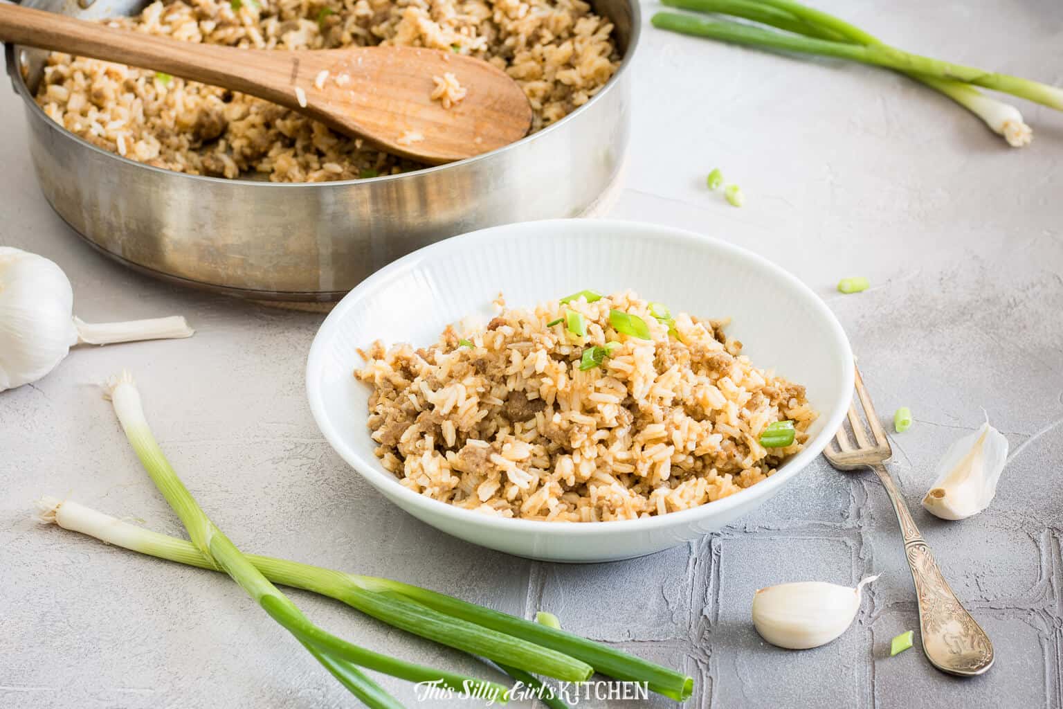 Horizontal image of Dirty Rice in bowl with scallions and garlic.