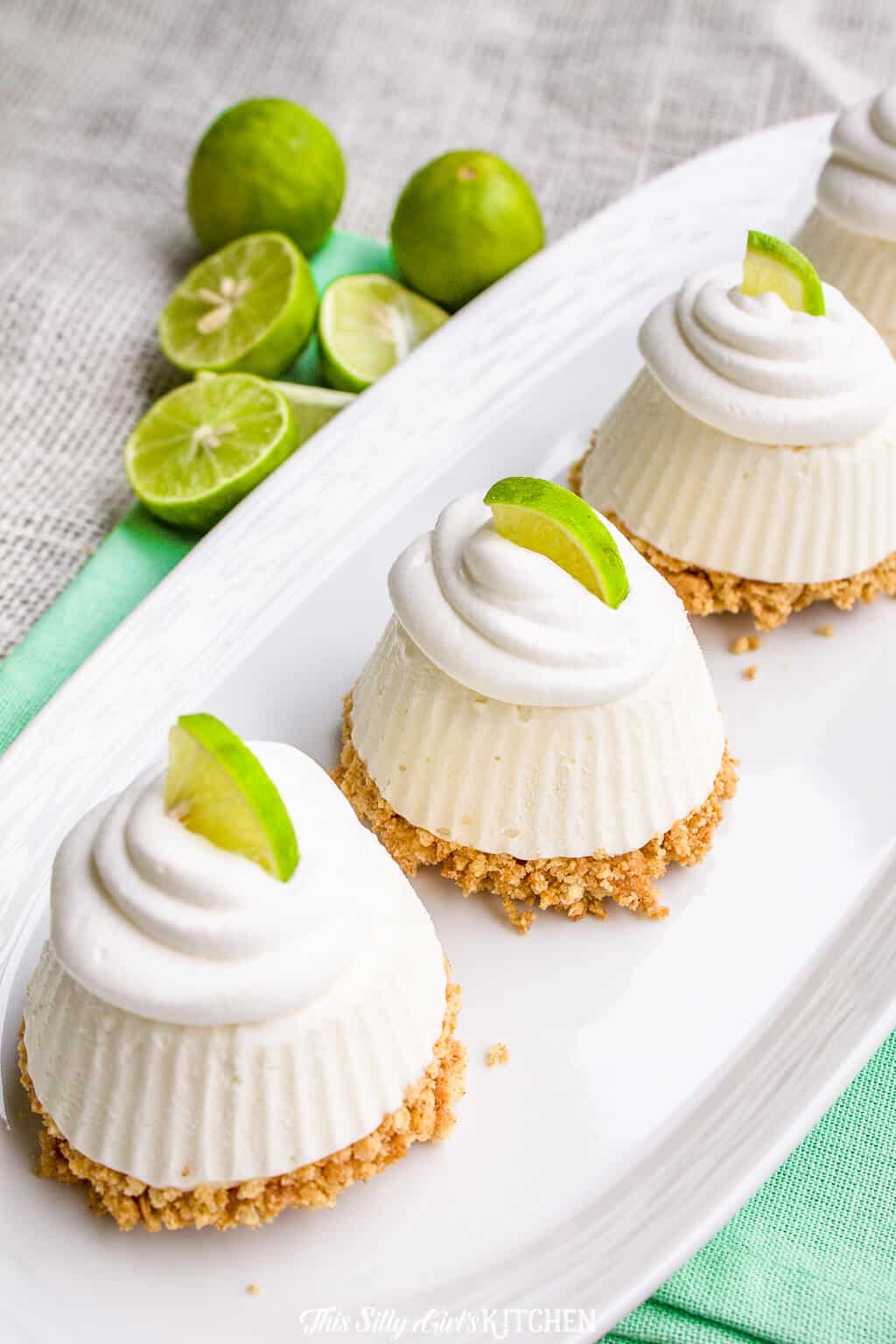 Overhead of Key Lime Pie on white plate topped with whipped topping and limes