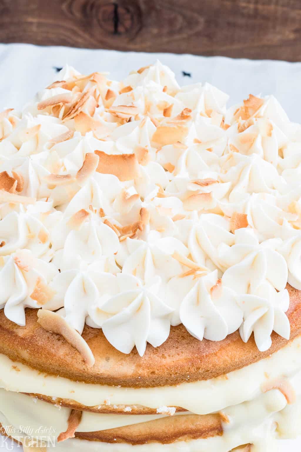 Naked Coconut Cake, layers of white cake, coconut pudding and coconut frosting, all topped with toasted coconut and caramel sauce! #Recipe from ThisSillyGirlsKitchen.com #coconut #coconutcake #cake #nakedcake
