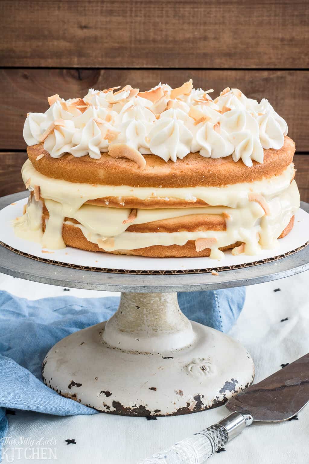Naked Coconut Cake, layers of white cake, coconut pudding and coconut frosting, all topped with toasted coconut and caramel sauce! #Recipe from ThisSillyGirlsKitchen.com #coconut #coconutcake #cake #nakedcake
