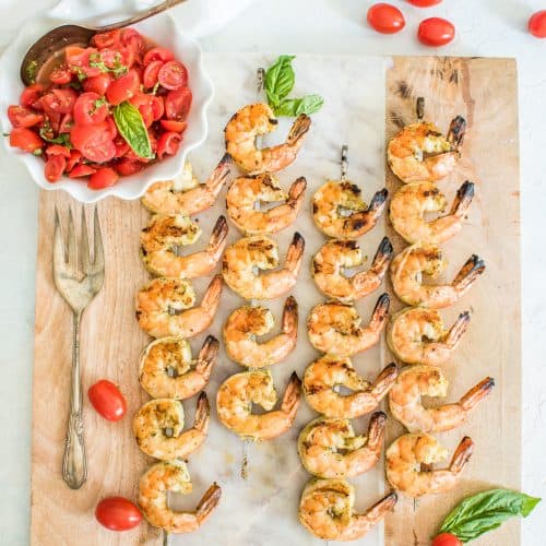 Grilled shrimp skewers on a board with fresh tomato basil bruschetta.