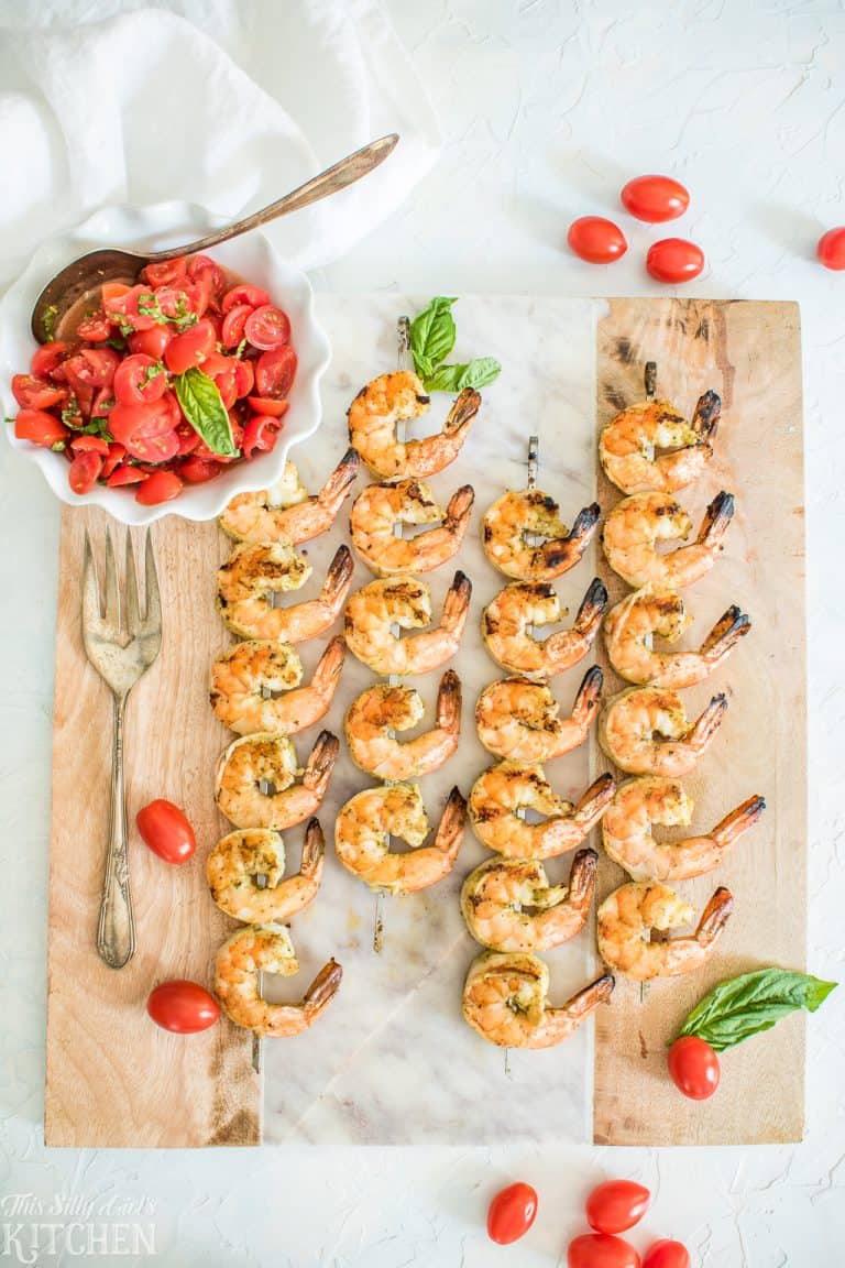Grilled shrimp skewers on a board with fresh tomato basil bruschetta.