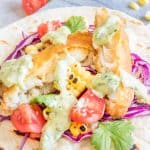 Creamy chimichurri fish taco sauce drizzled generously over a crispy fish taco on a white plate.