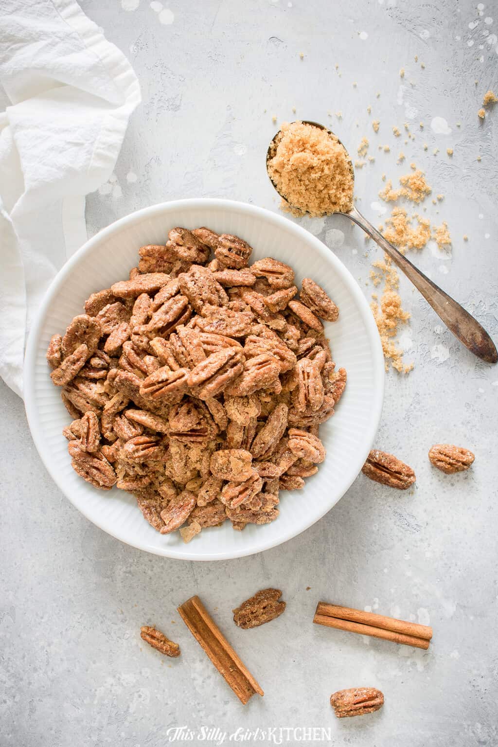 Cinnamon Sugar Roasted Pecans, sweet, crunchy, extremely easy and totally addicting! #Recipe from ThisSillyGirlsKitchen.com #pecans #candiedpecans #roastedpecans #cinnamon Overhead of Roasted Pecans in bowl with cinnamon and spoon of brown sugar