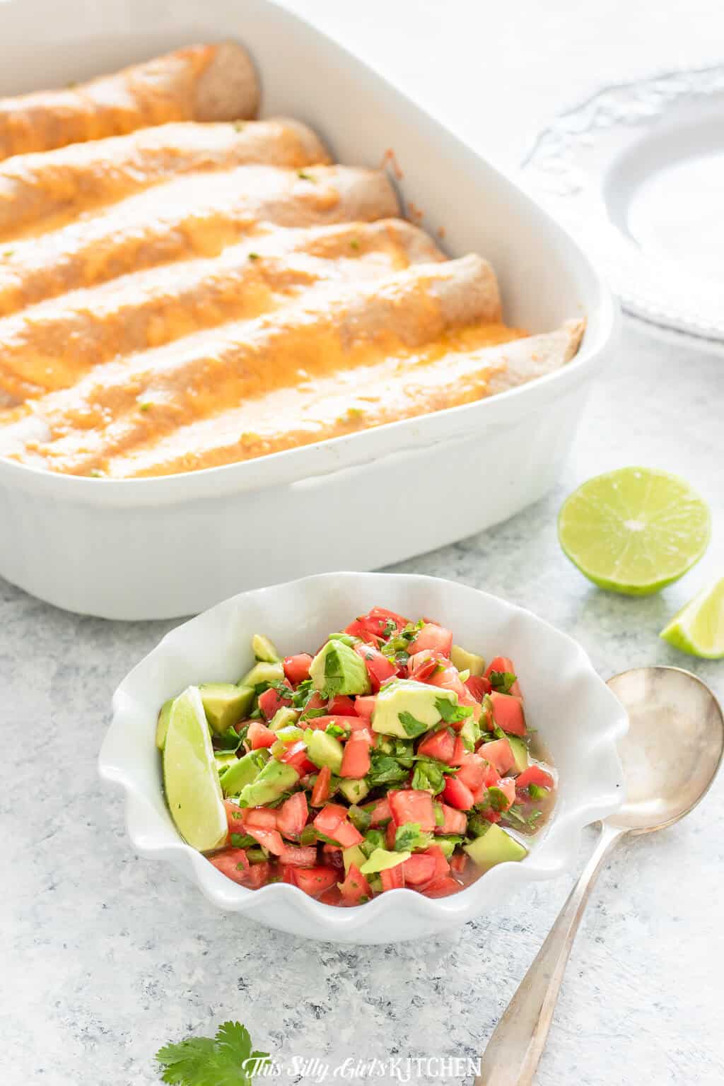 Salsa in white bowl in font of a pan of enchiladas