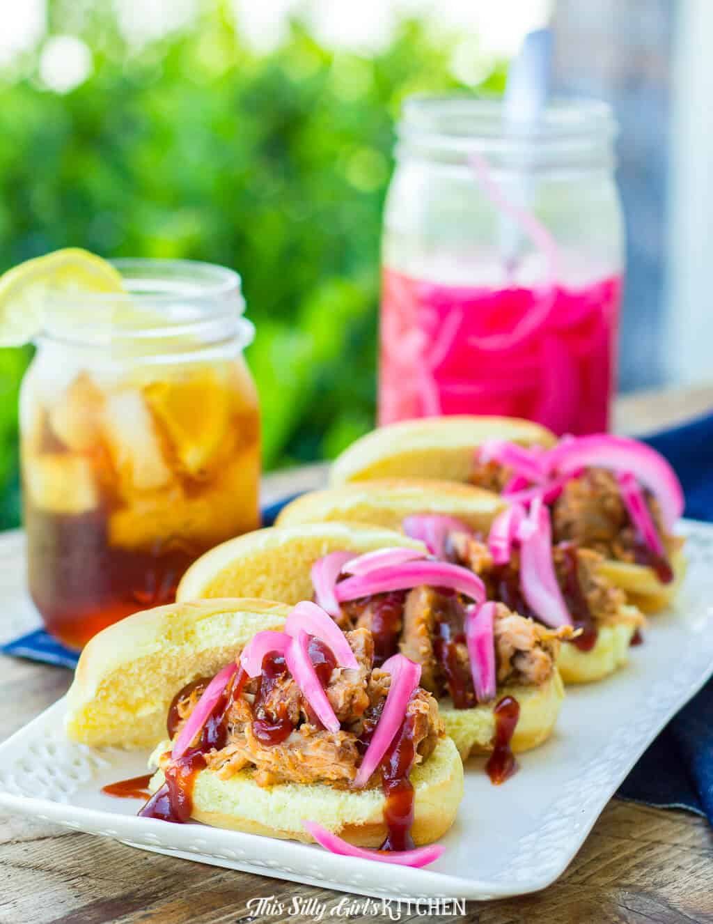 Pulled Pork Sliders on white platter in row topped with pickled onions