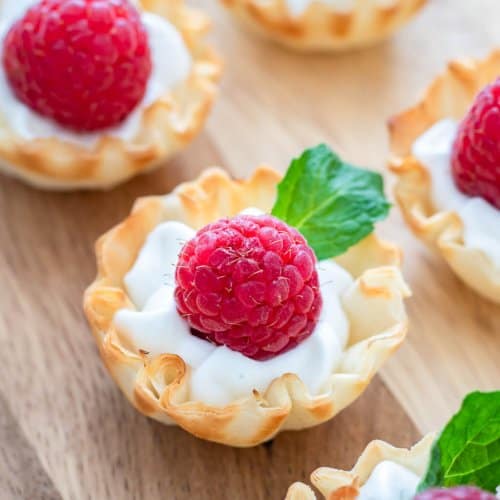 Raspberry Dessert Cups with lemon whipped cream, a fresh raspberry, and mint in a phyllo cup.