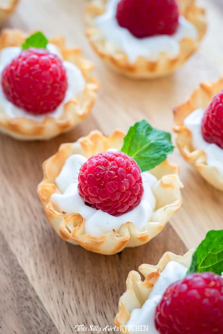 Raspberry Dessert Cups with lemon whipped cream, a fresh raspberry, and mint in a phyllo cup.
