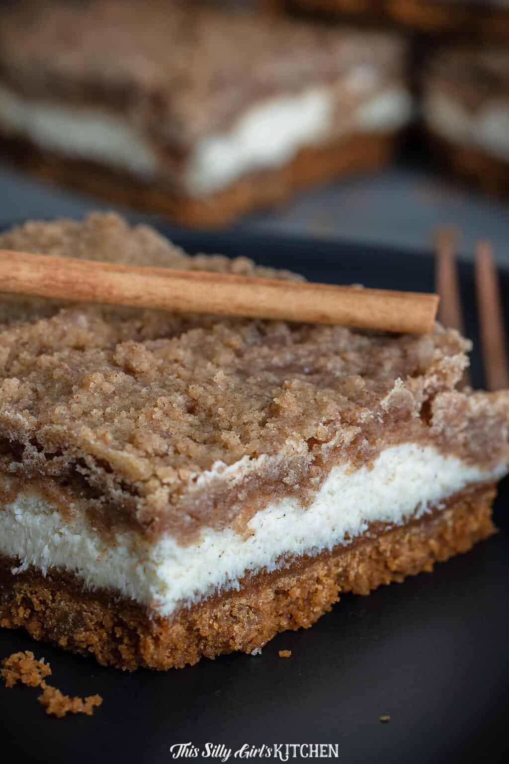 Close up of layers of bars on black plate topped with cinnamon stick.