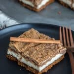 Snickerdoodle cheesecake bars stacked on a plate showing the Biscoff crust, creamy cinnamon cheesecake, and brown sugar crumble.