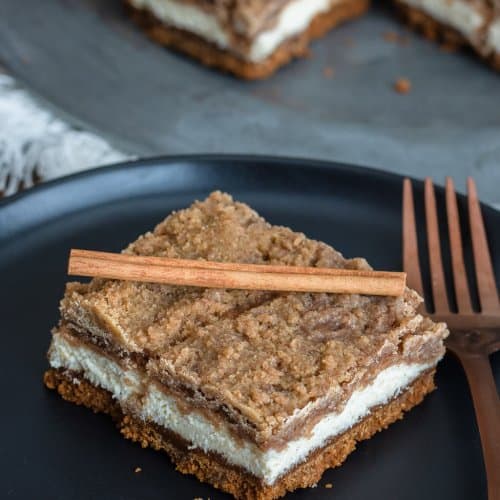 Snickerdoodle cheesecake bars stacked on a plate showing the Biscoff crust, creamy cinnamon cheesecake, and brown sugar crumble.