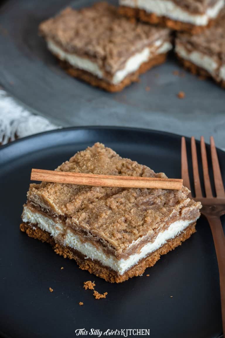 Snickerdoodle cheesecake bars stacked on a plate showing the Biscoff crust, creamy cinnamon cheesecake, and brown sugar crumble.
