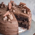 A whole chocolate layer cake with whipped chocolate frosting and chocolate shavings, one slice cut to show the moist layers.