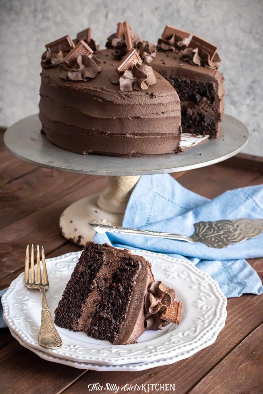 Chocolate Layer Cake on cake stand with slice missing which is on white plate