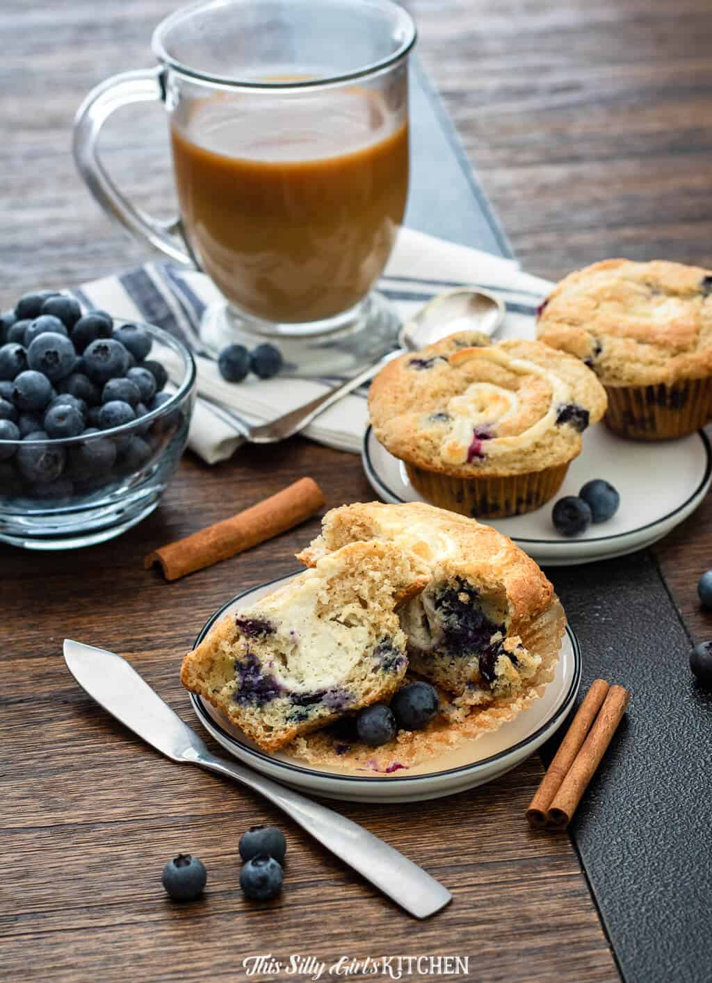 Muffins on plate with one split muffin and coffee and blueberries in background.