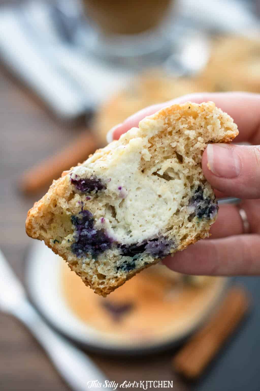Hand holding up half of a Best Blueberry Muffin showing cream cheese filling.