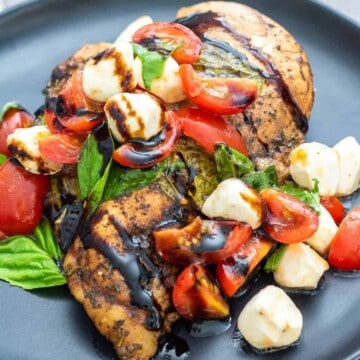 Sous vide chicken breast topped with cherry tomatoes, mozzarella, fresh basil, and balsamic glaze on a dark plate.