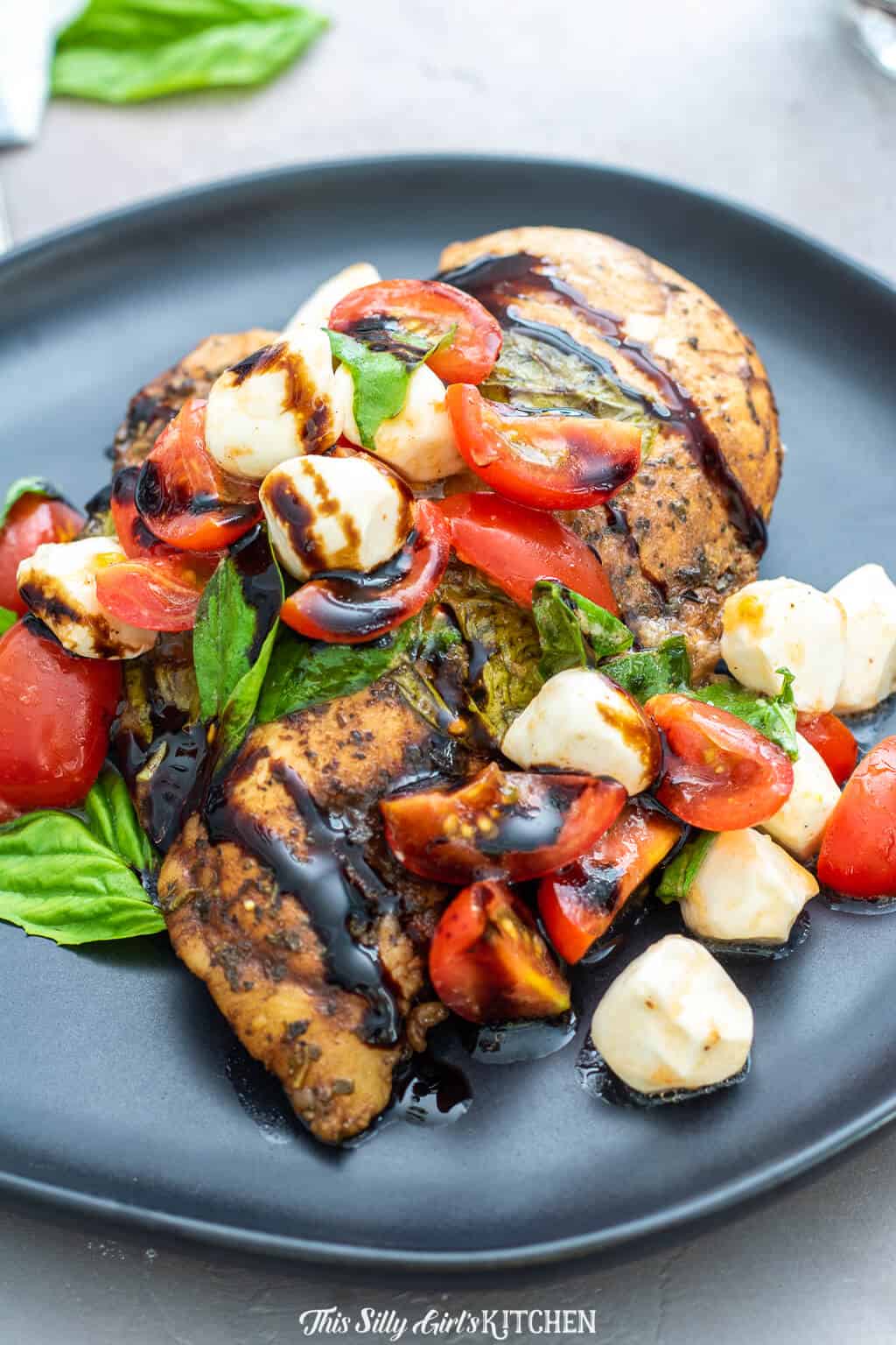 Sous Vide Chicken ion black plate topped with caprese salad