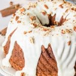 A glazed apple cinnamon coffee cake bundt topped with chopped pecans on a white plate.