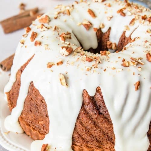A glazed apple cinnamon coffee cake bundt topped with chopped pecans on a white plate.