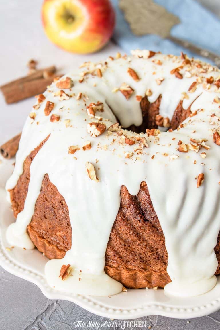 A glazed apple cinnamon coffee cake bundt topped with chopped pecans on a white plate.