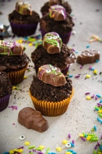 Halloween Cupcakes topped with cookie crumbs and candy splattered chocolate skulls on a gray counter.