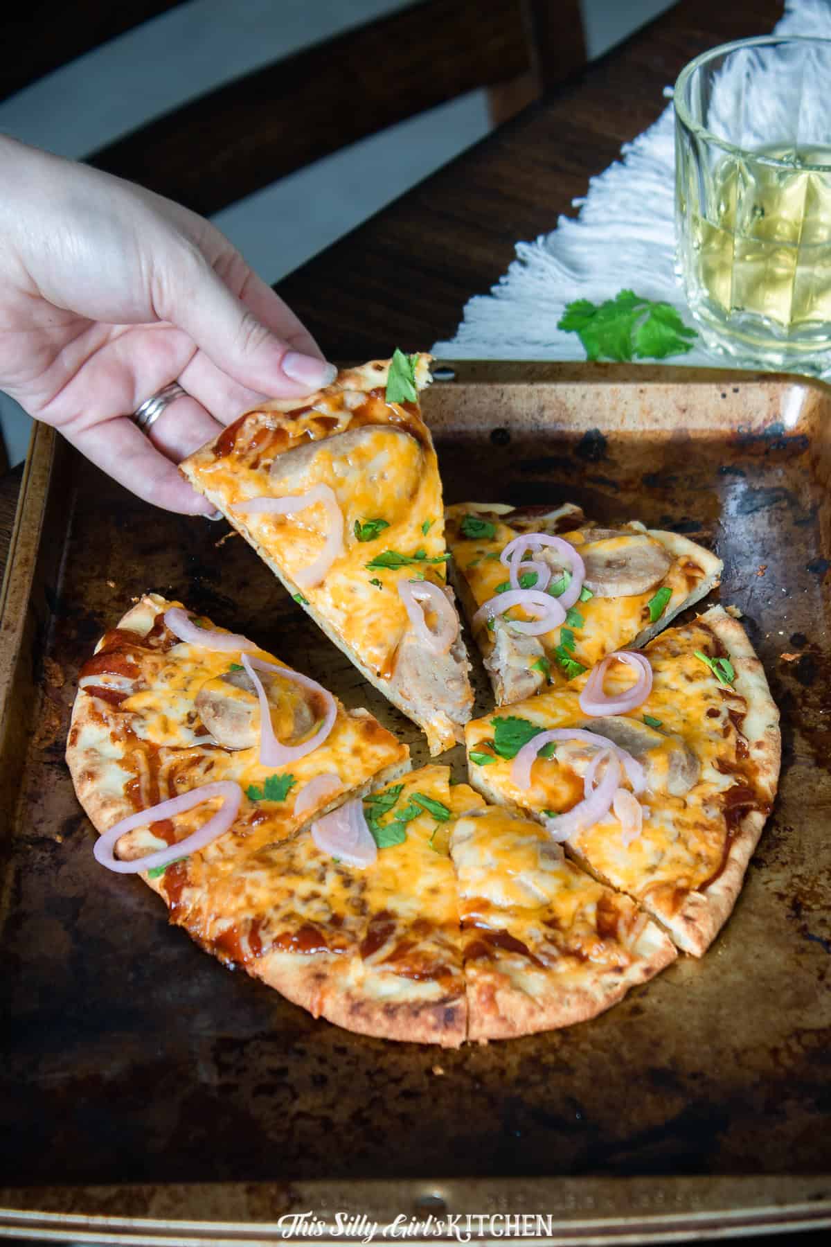 A hand lifting a slice of BBQ chicken pizza with melty cheese stretching.